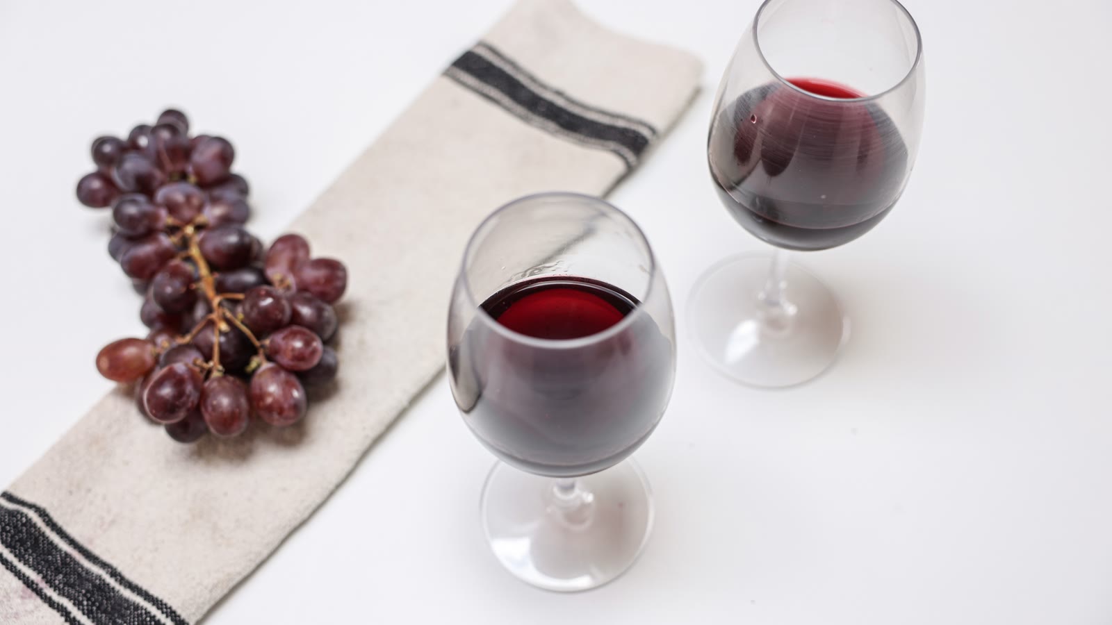 To glas rødvin og druer på hvid dug