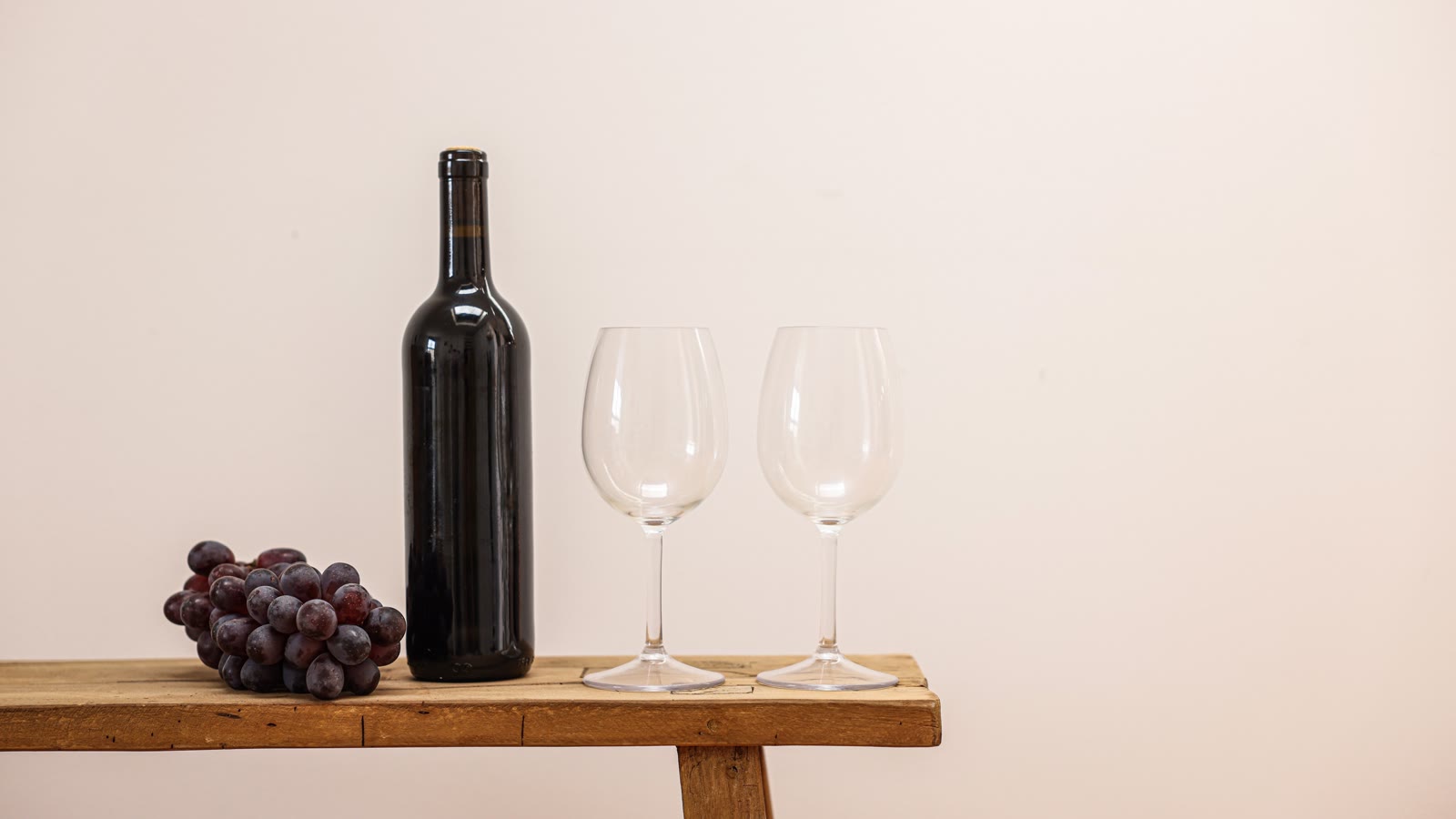 Vinflaske, to glas og druer på en træbænk
