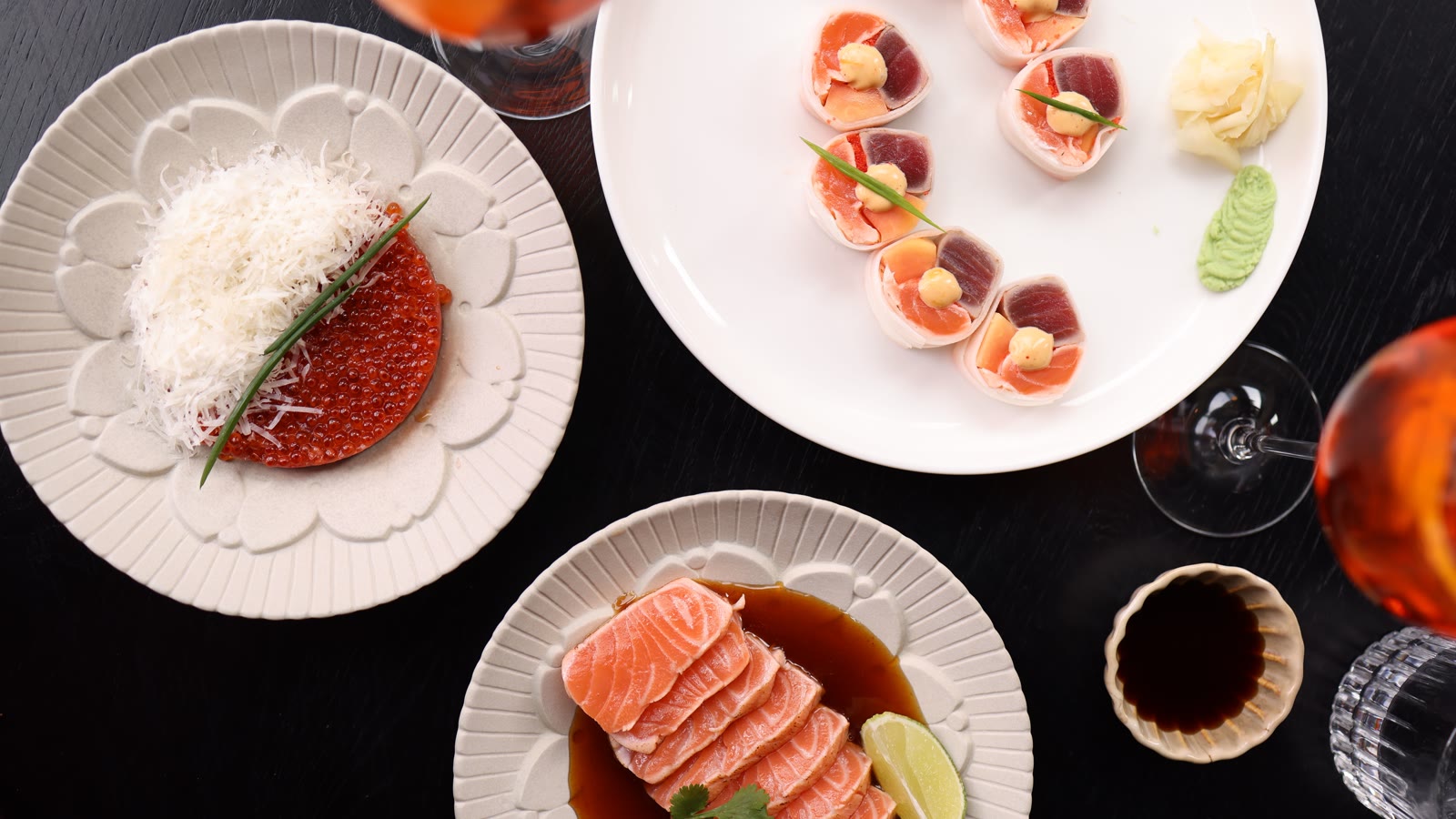 Sushi og sashimi anrettet på tallerkener med et vinglas ved siden af